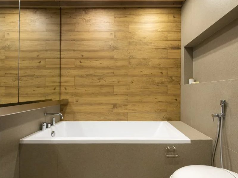 Baño con revestimiento porcelánico efecto madera colocado sobre el azulejo existente y bañera empotrada