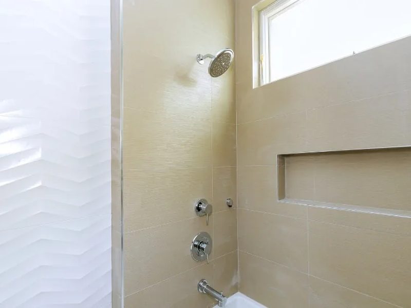 Ducha de obra alicatada con mampara de vidrio en el hueco de una antigua bañera