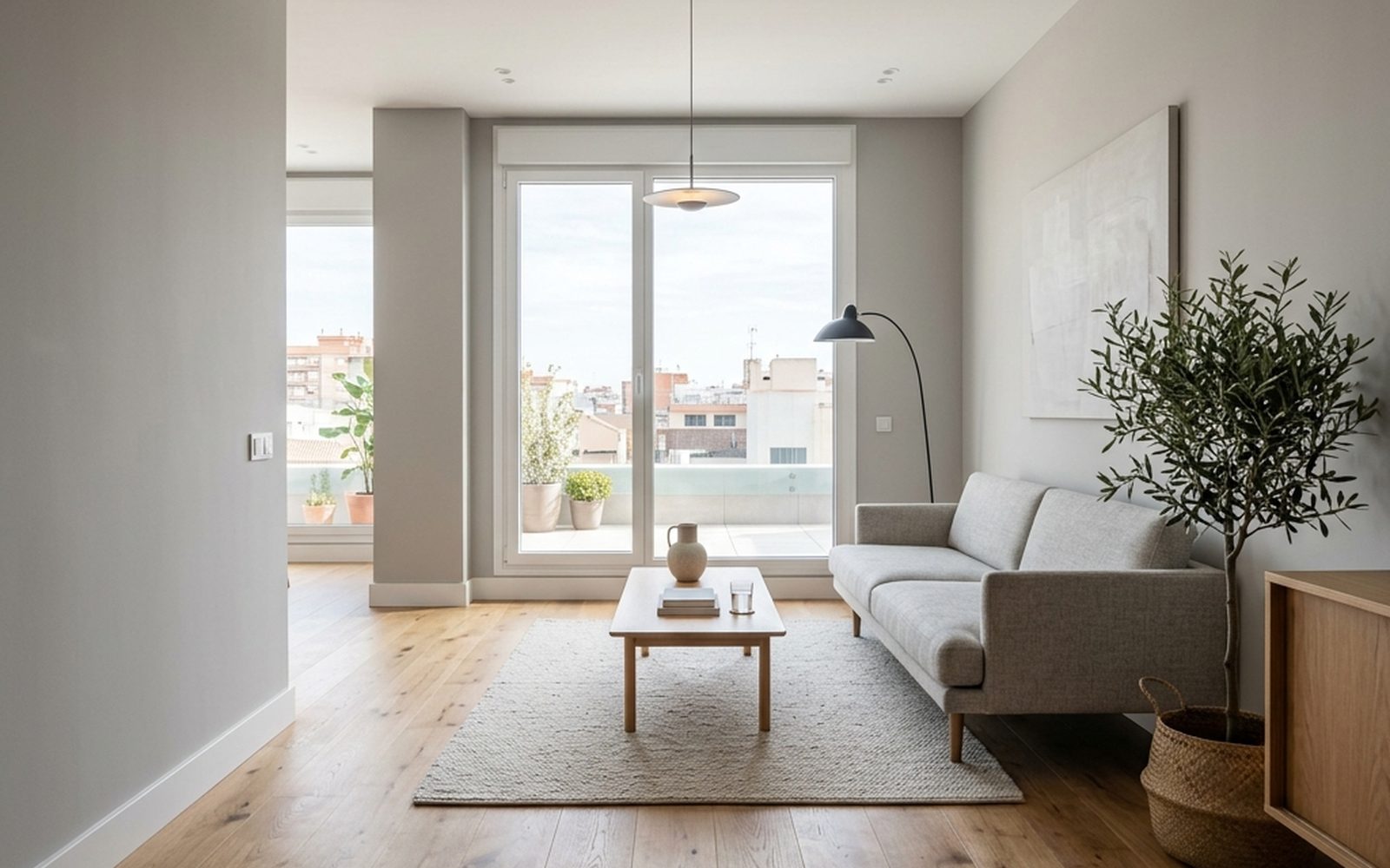 Salón luminoso de un piso reformado con suelo de madera clara, sofá blanco y balcón