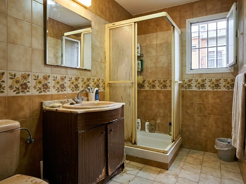 Baño antes de la reforma: alicatado beige con cenefa de flores, plato de ducha elevado y mueble de madera oscura
