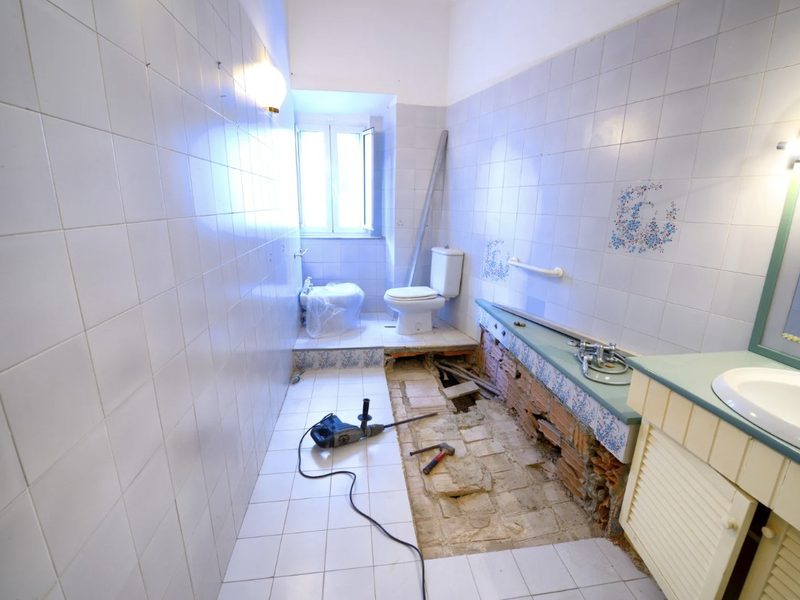 Baño en obra con la bañera retirada, el suelo levantado y herramientas sobre el alicatado