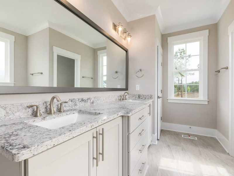 Baño reformado con encimera de granito, doble lavabo bajo encimera y espejo de pared completa