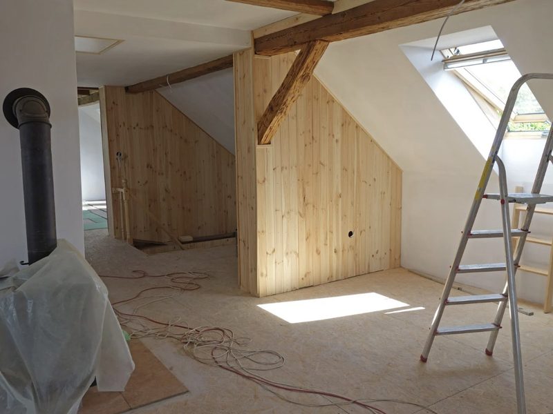 Buhardilla de un chalet en reforma con revestimiento de madera, ventana de tejado y vigas vistas