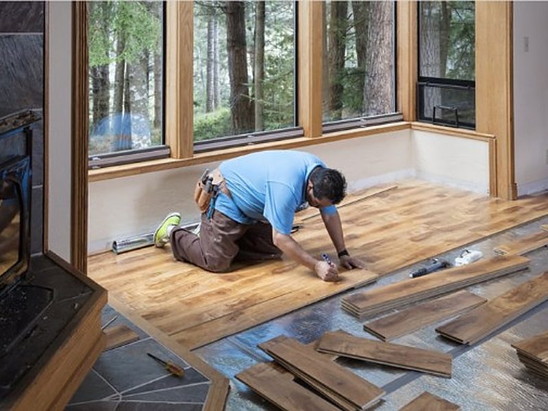 Instalador colocando un suelo de madera junto a grandes ventanales en una vivienda