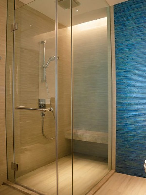 Ducha con mampara de vidrio, banco de obra, iluminación empotrada y pared de azulejo azul
