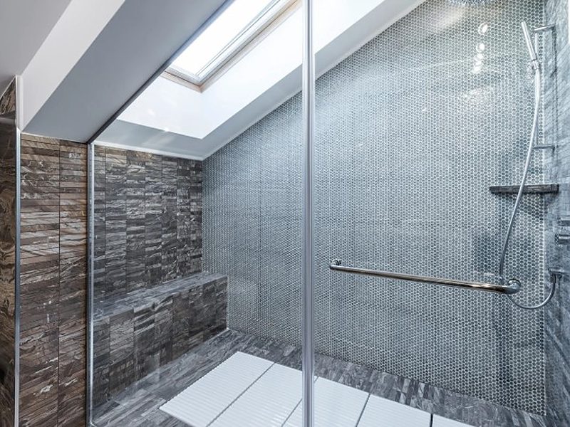 Ducha de obra amplia con banco, barra de apoyo, mosaico gris y claraboya en el techo