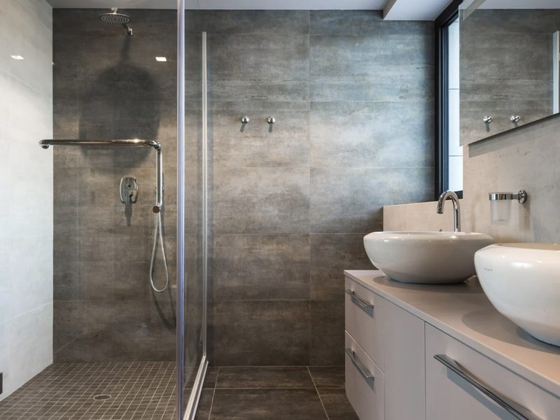 Baño con ducha walk-in de vidrio, porcelánico gris de gran formato y doble lavabo sobre encimera